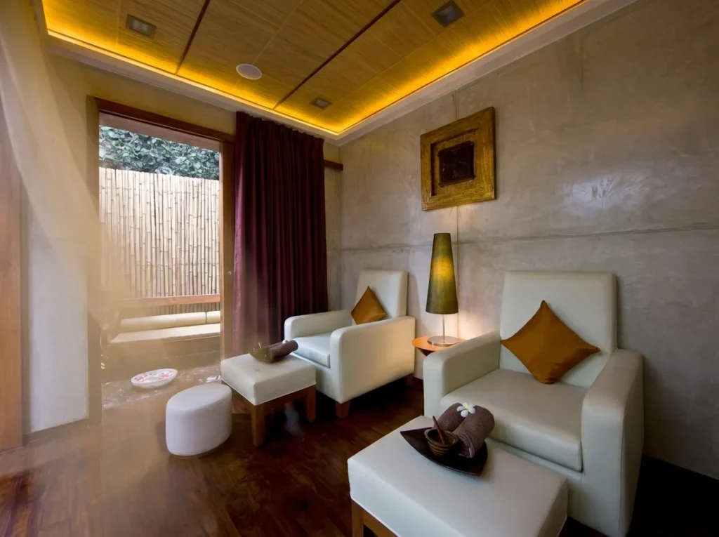 Private spa relaxation room interior construction in Bangalore with white lounge chairs, bamboo courtyard view, amber cove lighting, and timber ceiling by High Tech Constructions