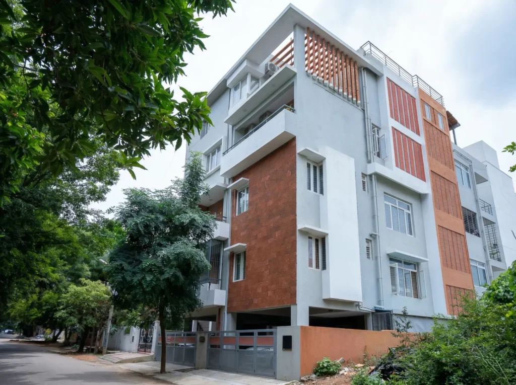 Contemporary multi-storey residential building with exposed brick cladding, terracotta louvers, and stilt parking in Bangalore.