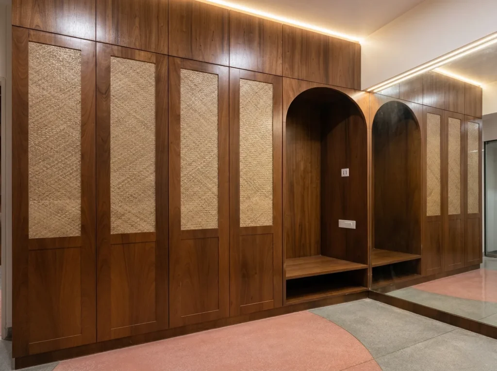 Full-height walnut wardrobe with cane panel inserts, arched alcove seating, and LED cove lighting — interiors and construction in Bangalore.